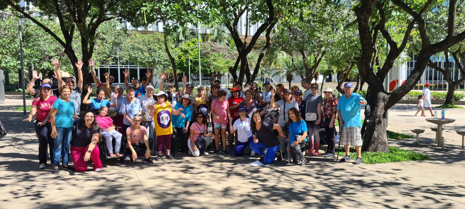 Grupo de pacientes idosos e profissionais reunidos ao ar livre, acenando para a câmera.